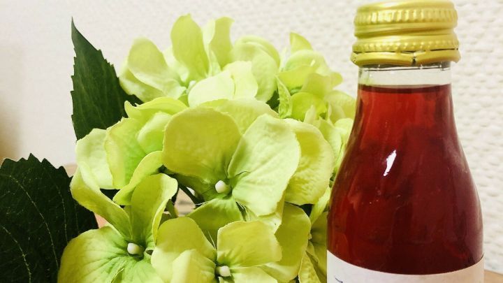 Ein Glas mit Johanniskraut&ouml;l steht neben einer bl&uuml;henden Pflanze, symbolisiert die DIY-Herstellung zur Linderung von Verbrennungen.