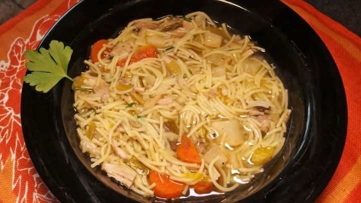 Eine schwarze Sch&uuml;ssel mit dampfender Suppe, gef&uuml;llt mit Nudeln, Gem&uuml;se und H&auml;hnchen, auf einem dekorativen Tischuntersetzer.