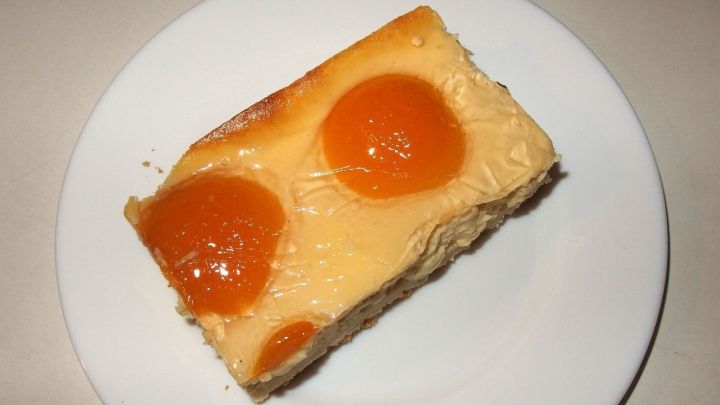 Ein St&uuml;ck gesunder Kuchen liegt auf einem wei&szlig;en Teller und zeigt gl&auml;nzende Aprikosenh&auml;lften, bereit zum Genie&szlig;en.