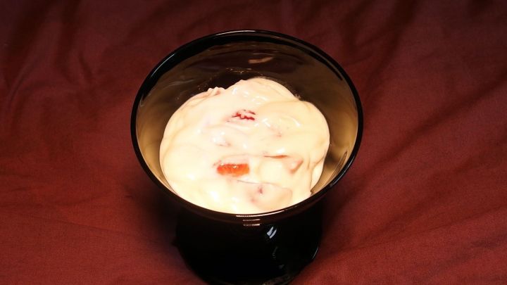 Eine schwarze Sch&uuml;ssel mit selbstgemachtem Fr&uuml;chtequark, gef&uuml;llt mit cremigem, fruchtigem Quark auf einem roten Untergrund.