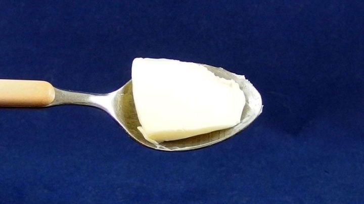 Ein L&ouml;ffel mit Butter steht im Vordergrund und zeigt, wie das Lebensmittel zur Linderung von Halsschmerzen eingesetzt werden kann.