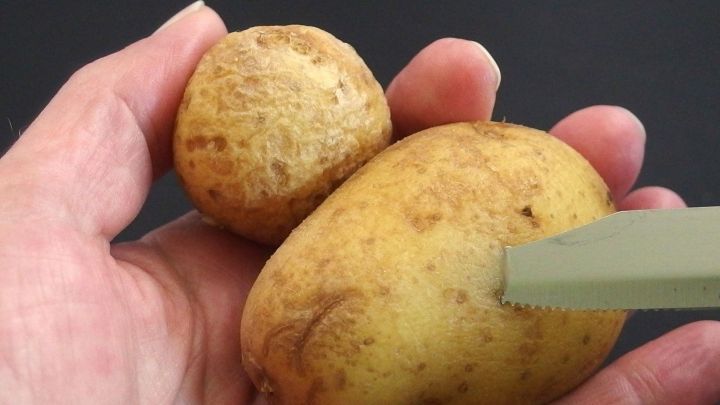 Zwei unterschiedlich gro&szlig;e Pellkartoffeln liegen in der Hand, w&auml;hrend ein Messer an die gr&ouml;&szlig;ere Kartoffel herangef&uuml;hrt wird.