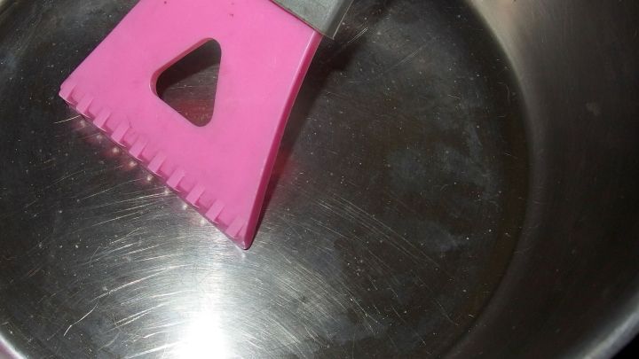 Ein Eiskratzer liegt auf einem gl&auml;nzenden Topfboden und entfernt m&uuml;helos eingebranntes Material.