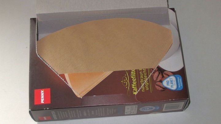 Ein ge&ouml;ffneter Kaffeefilterkarton mit einem Kaffeefilter, der sich bereit ist zum Gebrauch darin befindet.
