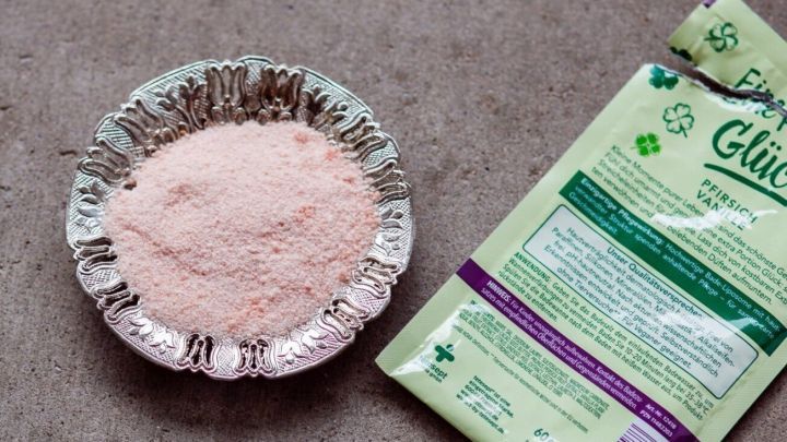 Badesalzkristalle liegen in einer kleinen Schale und eine offene Verpackung zeigt die Produktdetails auf einem neutralen Hintergrund.