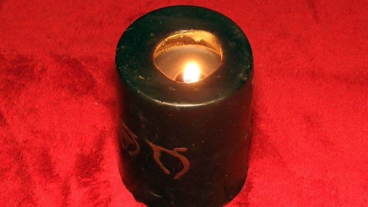 Eine brennende Kerze aus gr&uuml;nem Wachs steht auf einem roten Tuch, m&ouml;glicherweise in einem gem&uuml;tlichen Raum, und k&ouml;nnte Wachsreste hinterlassen.