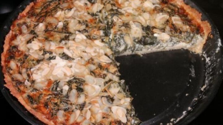 Eine Quiche mit Spinat und Gorgonzola liegt auf einem Teller, ein St&uuml;ck wurde herausgenommen, um sie zu servieren.