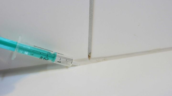 Eine Spritze injiziert Fl&uuml;ssigkeit in Fugen von wei&szlig;en Fliesen, um Kalkablagerungen zu entfernen.