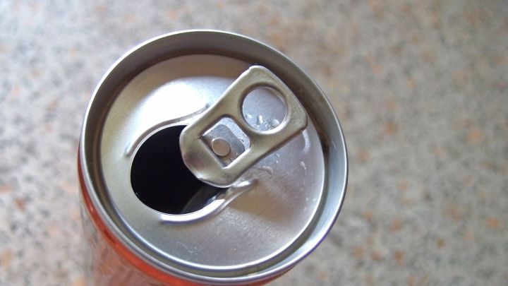 Eine Cola- oder Limonadendose mit ge&ouml;ffnetem Verschluss steht auf einer einfarbigen Oberfl&auml;che, bereit zum Trinken.