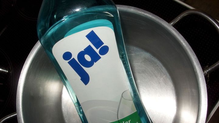 Eine Flasche Klarsp&uuml;ler steht im Inneren eines metallenen Topfes und k&ouml;nnte helfen, Angebranntes zu l&ouml;sen.