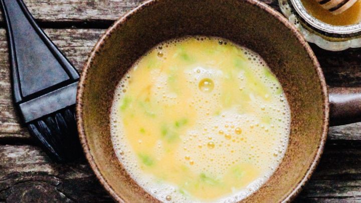 Eine Sch&uuml;ssel mit einer gelben Mischung aus Avocado und anderen Zutaten steht auf einem Holztisch, neben einem Glas Honig.