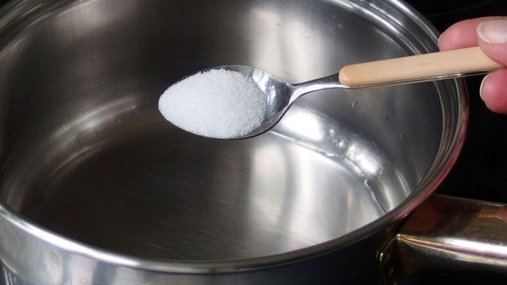 Ein L&ouml;ffel Zucker wird &uuml;ber einem Topf mit Wasser gehalten, w&auml;hrend die Zubereitung von Milchspeisen beginnt.