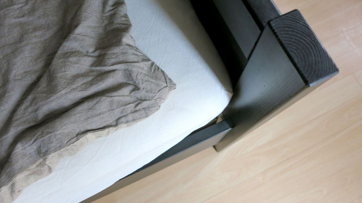 Ein straffes Bettlaken liegt &uuml;ber einer Matratze in einem modernen Schlafzimmer mit einem Holzfu&szlig;boden.