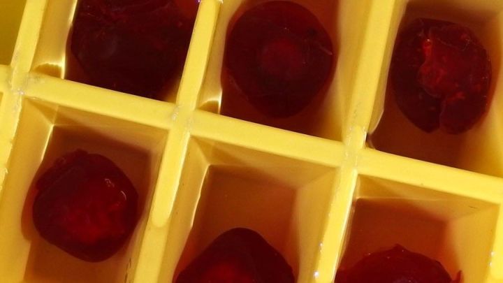 Kugelf&ouml;rmige, rote Eisw&uuml;rfel liegen in einem gelben Eisw&uuml;rfelformer in einer k&uuml;hlen Umgebung, bereit zum Servieren.