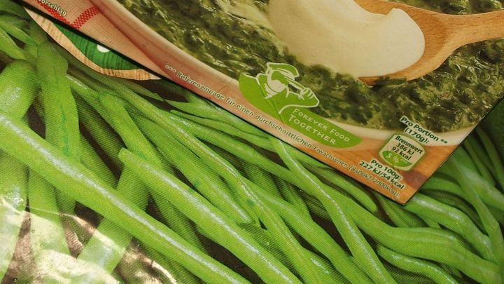 Gr&uuml;ne Bohnen und eine Verpackung mit Sahne sind auf einem gefrorenen Gem&uuml;sebett sichtbar, was Tiefk&uuml;hlgem&uuml;se pr&auml;sentiert.