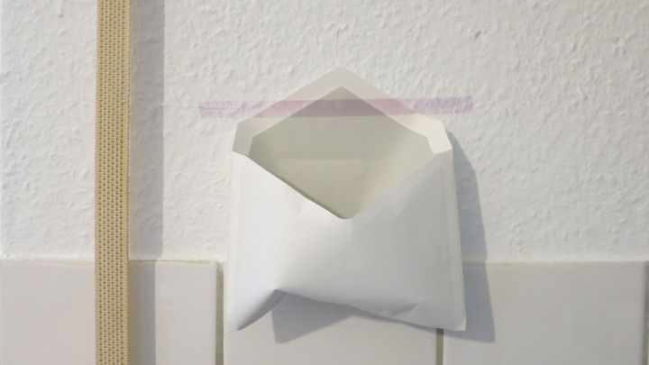 Ein leeres, wei&szlig;es Briefkuvert ist an der Wand befestigt, w&auml;hrend ein Werkzeug f&uuml;r die staubfreie Bearbeitung daneben h&auml;ngt.