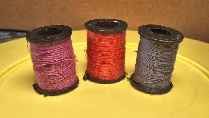 Drei Spulen mit N&auml;hgarn in verschiedenen Farben stehen auf einer gelben Unterlage, bereit zum Organisieren und Benutzen.