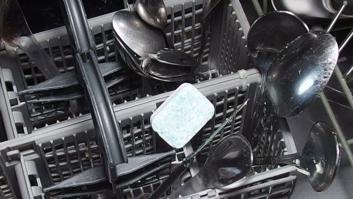 Ein Besteckkorb im Geschirrsp&uuml;ler enth&auml;lt verschiedene L&ouml;ffel und einen Geschirrsp&uuml;ltab, der zwischen den Utensilien liegt.