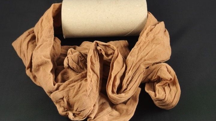 Ein zusammengerollter Pappkern liegt mittig umgeben von einer zerkn&uuml;llten Strumpfhose in einem dunklen Umfeld.