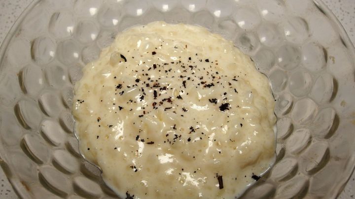 Eine Sch&uuml;ssel Milchreis, die mit einer Prise schwarzem Pfeffer garniert ist, steht auf einem glatten Tisch.