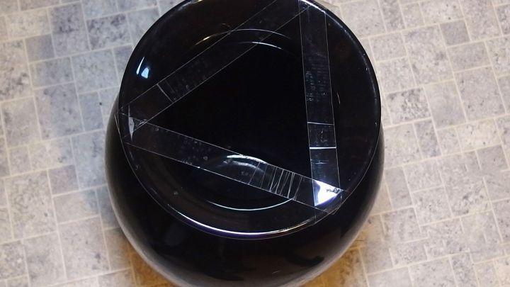 Eine schwarze Vase mit einer breiten &Ouml;ffnung steht auf einem hellen, gemusterten Untergrund, bereit, dekoriert zu werden.