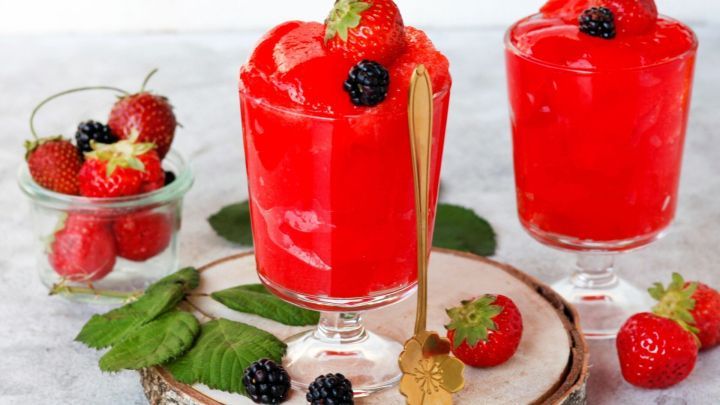 Rotes, alkoholfreies Sorbet in gl&auml;sernen Schalen wird mit Beeren und einem goldenen L&ouml;ffel auf einem Holzbrett serviert.