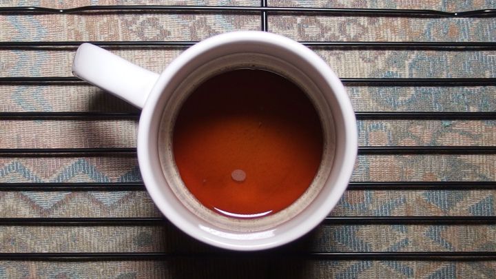 Ein Kaffeebecher steht auf einem Grillrost. Der Kaffee zeigt eine tiefbraune Farbe und steht ruhig in der Tasse.