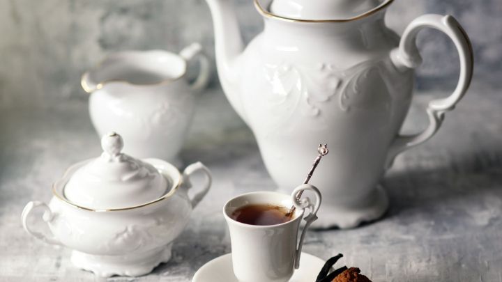 Eine elegante Teekanne mit Tassen und Zuckergef&auml;&szlig; steht auf einem hellen, strukturierten Untergrund, bereit zum Servieren.