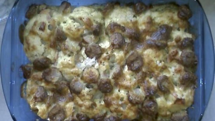 Auflauf in einer Glasform mit knusprig gebr&auml;unten Bratwurstst&uuml;cken und geschmolzenem K&auml;se, auf einem K&uuml;chentisch serviert.