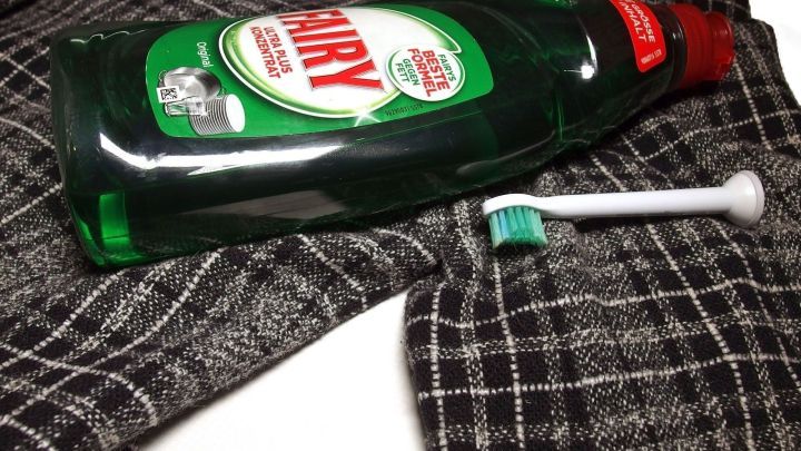 Ein gr&uuml;ner Flaschen mit Sp&uuml;lmittel liegt auf einem karierten Anzug, daneben eine kleine Zahnb&uuml;rste f&uuml;r die Reinigung.