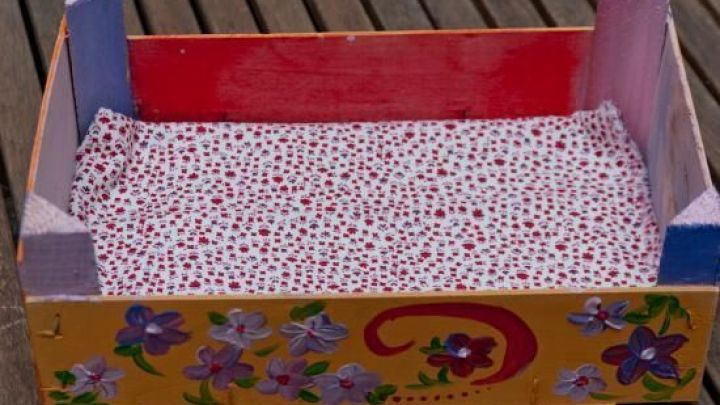 Ein kleines Serviertablett aus einer Erdbeerkiste, bunt bemalt mit Bl&uuml;tenmuster, steht auf Holzboden.