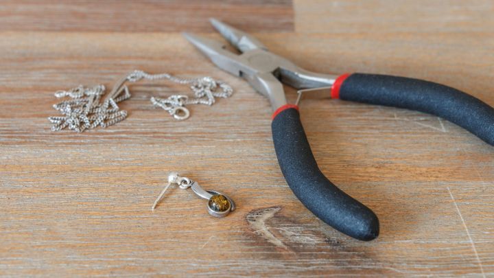 Ein Ohrstecker liegt neben einer Zange und Kette auf einem Holztisch, bereit zur Umgestaltung als Anh&auml;nger.