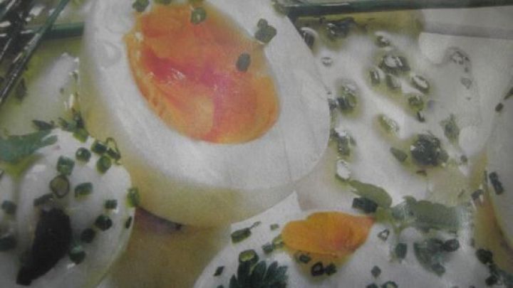 Eier in Scheiben, garniert mit Kr&auml;utervinaigrette, liegen appetitlich angerichtet auf einem Teller.