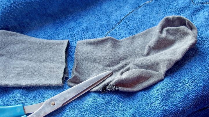 Eine Schere schneidet eine besch&auml;digte Strumpfhose auf einem blauen Stoff, um sie in eine Leggins umzuwandeln.