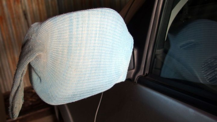 Ein frostsicherer Autospiegel ist mit einem blauen Tuch abgedeckt, w&auml;hrend er an einem geparkten Auto befestigt ist.