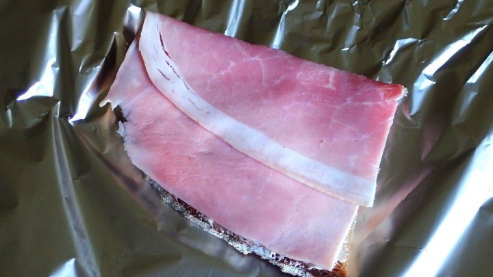 Ein St&uuml;ck Schinken liegt auf einer Aluminiumfolie, bereit f&uuml;r die eingebaute K&uuml;hlung im Pausenbrot in einer K&uuml;che.
