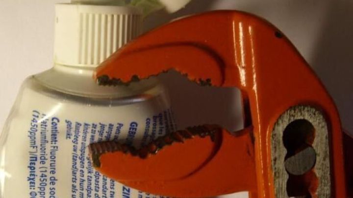 Ein orangefarbener Schraubenschl&uuml;ssel dr&uuml;ckt eine Tuben&ouml;ffnung zusammen, um die Tube vollst&auml;ndig auszudr&uuml;cken.