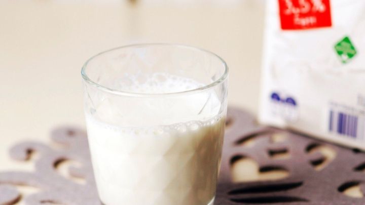 Ein Glas mit Milch steht auf einem Tisch, w&auml;hrend eine Tetrapackt&uuml;te im Hintergrund sichtbar ist.