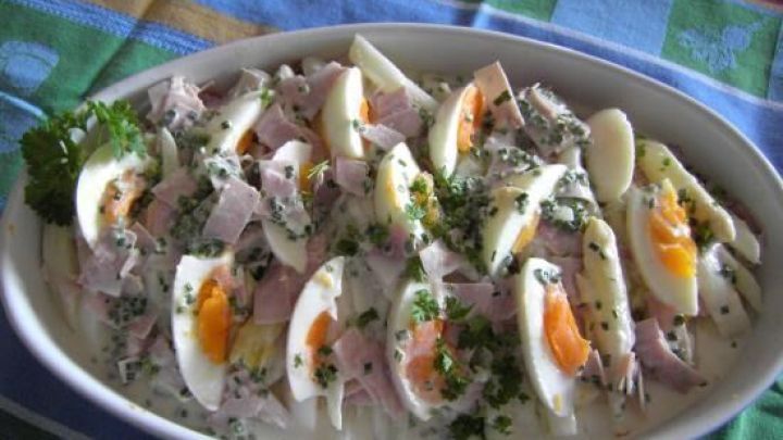 Spargelsalat mit Eiern und Schinken in Sahnesauce, garniert mit Petersilie, serviert auf einer bunten Tischdecke.