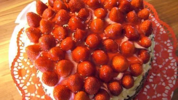 Eine Erdbeersahnetorte mit frischen, gl&auml;nzenden Erdbeeren ist auf einem filigranen, roten Tortenuntersetzer platziert.