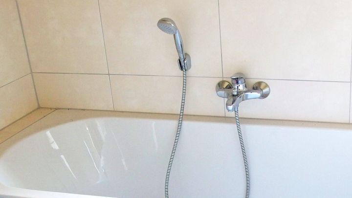 Eine Badewanne mit Wasserhahn und Brause, bereit zum Duschen, um Seifenreste zu reduzieren, steht in einem hellen Badezimmer.