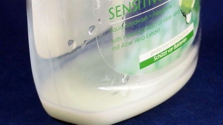 Eine halb leere Flasche Fl&uuml;ssigseife steht auf einem blauen Hintergrund, mit Resten des Badeschaums sichtbar im Inneren.