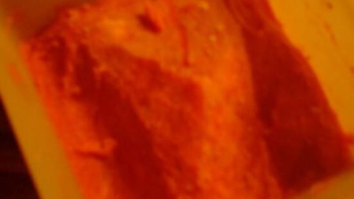 Eine Plastikschale enth&auml;lt rosafarbenes Erdbeereis. Die Aufnahme erfolgt bei schwachem Licht auf einem gestreiften Tisch.