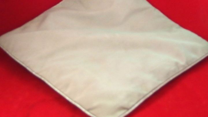 Ein quadratisches Kissen liegt auf einem roten Untergrund und zeigt die Nutzung von Kissenf&uuml;llung aus Stoffresten.