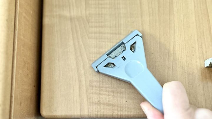 Ein Handwerker entfernt Fettbelag mit einem Schaber von einer Holzoberfl&auml;che in einer modernen K&uuml;che.