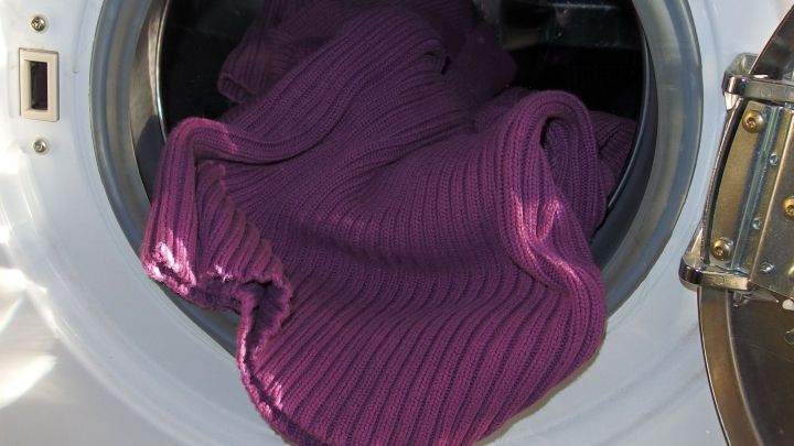 Ein lila Pullover liegt in einer Waschmaschine, die gerade l&auml;uft, symbolisiert modernes W&auml;schewaschen heute.