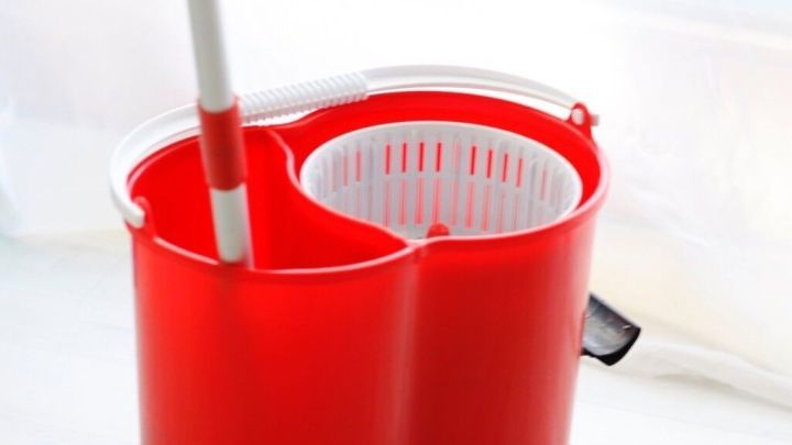 Ein roter Wischeimer steht auf einem hellen Boden, bereit, mit kaltem Wasser gewischt zu werden.