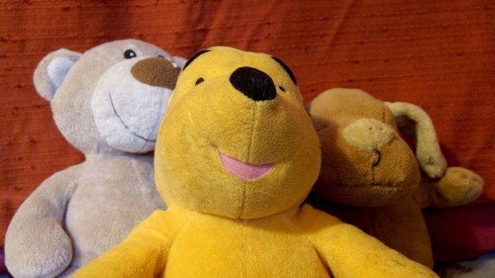 Bunte Stofftiere stehen l&auml;chelnd nebeneinander auf einem orangefarbenen Hintergrund, die perfekte Darstellung von Kinderkleidung und Spielsachen.