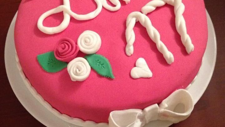Ein runder Kuchen mit pinkem Marshmallow-Fondant ist dekoriert mit dem Namen "Lini" und der Zahl "17", umgeben von Zuckerrosen.
