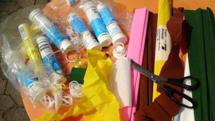 Brausetablettenh&uuml;lsen werden vorbereitet, um als H&auml;ngebeh&auml;lter f&uuml;r Blumen zu dienen. Umgeben von Bastelmaterialien auf einem Tisch.